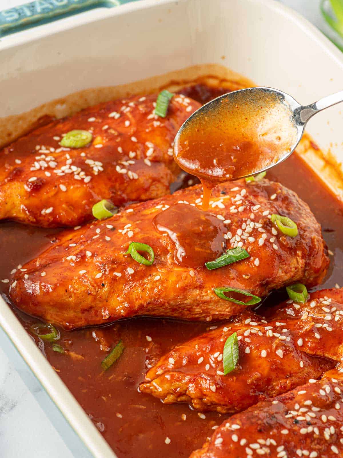 Spooning honey sriracha sauce over baked chicken breast.