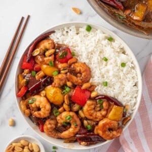 Kung pao shrimp recipe in a bowl with rice and chopsticks on the rice.