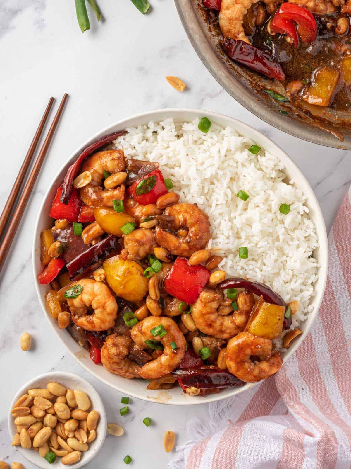 Kung pao shrimp recipe in a bowl with rice and chopsticks on the rice.