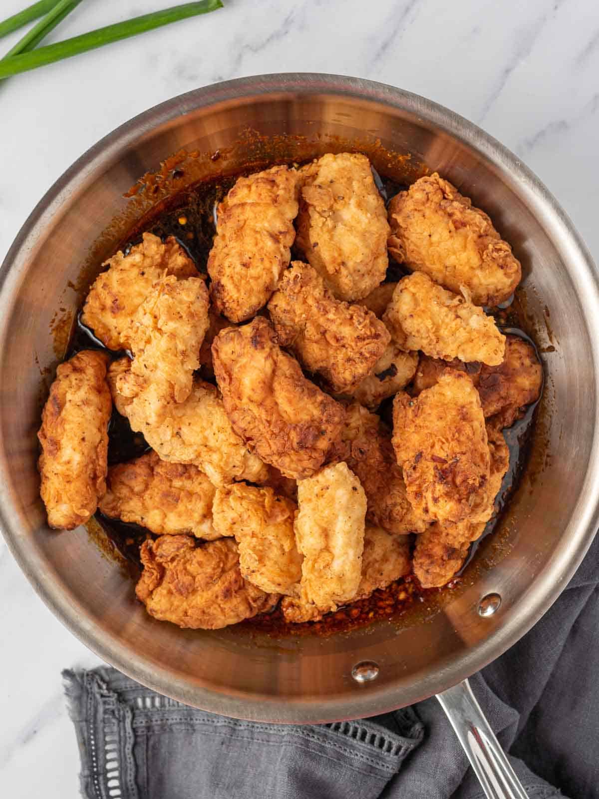 Coating crispy chicken tenders with korean chicken sauce in a pan.
