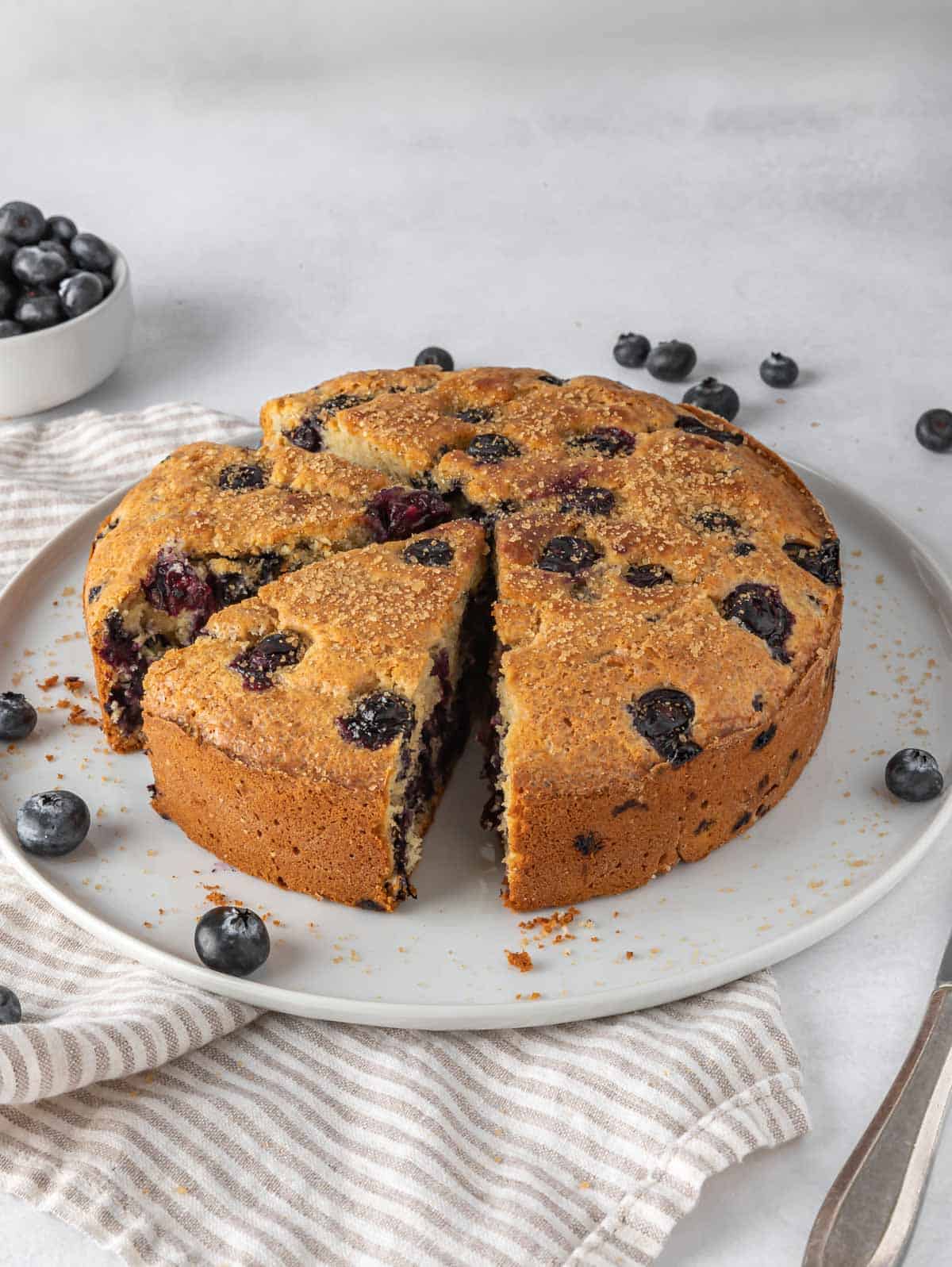 Sliced blueberry breakfast cake on a platter with fresh blueberries.