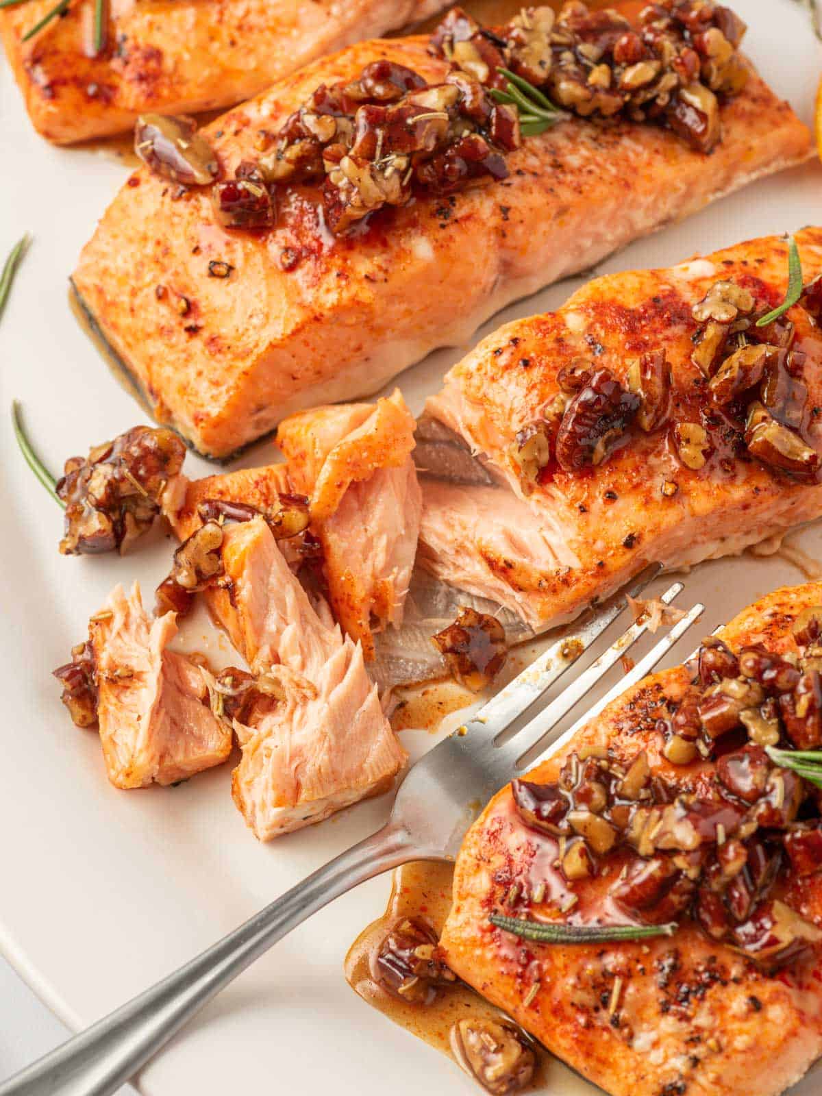 A flaky piece of salmon with maple syrup and pecans on a plate with a fork.