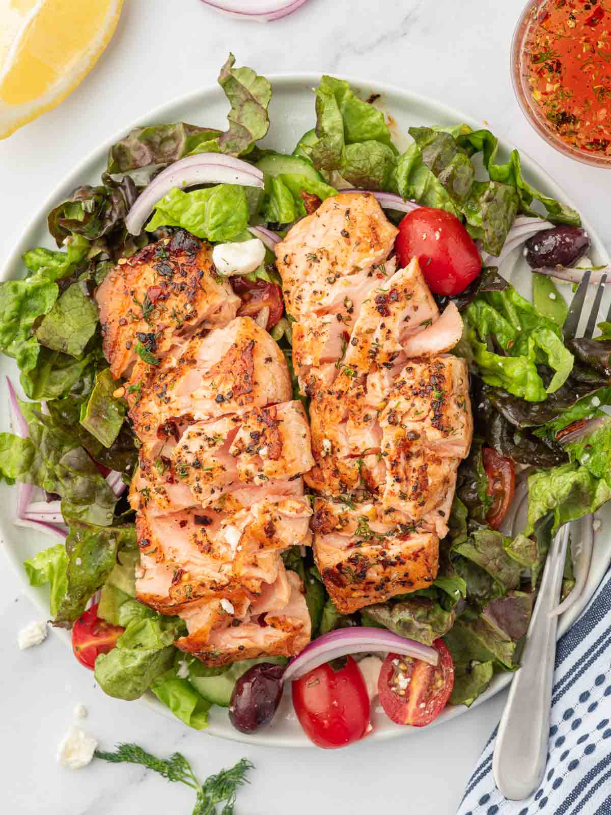 A plate of greek salad with grilled salmon and a fork.