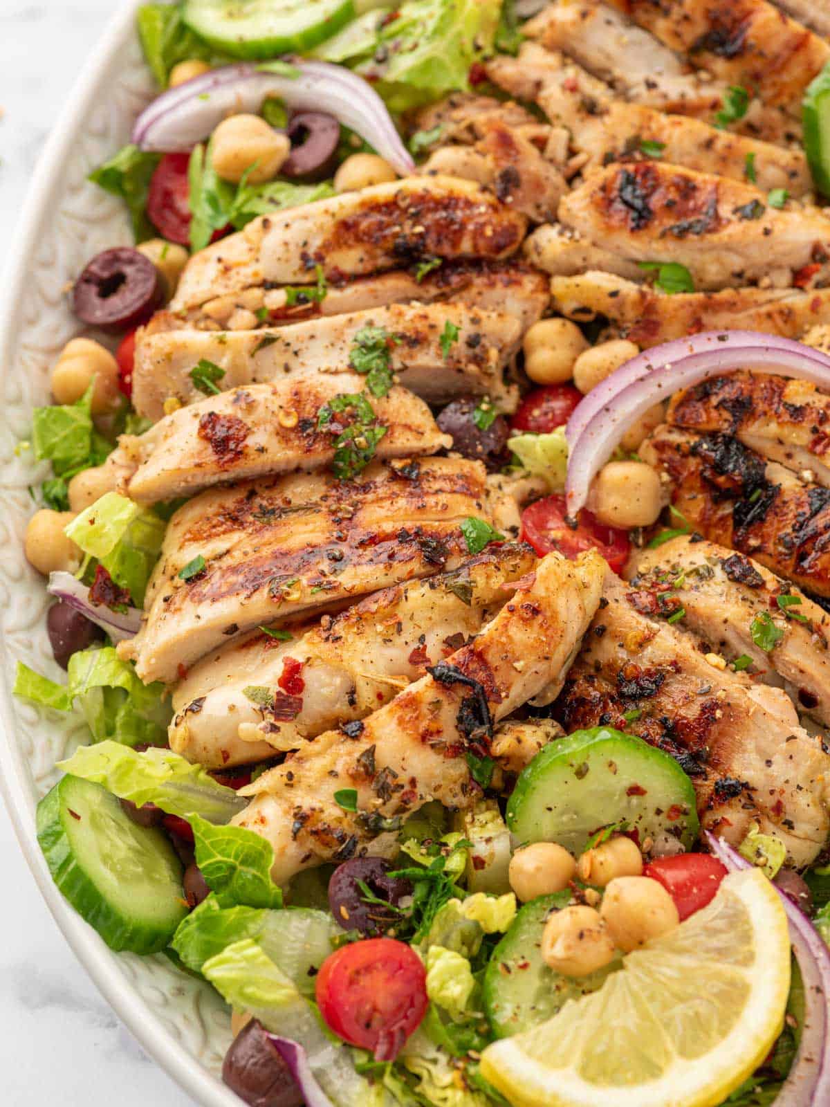 A big platter of mediterranean salad topped with lemon herb chicken.