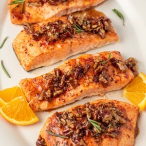 Salmon with pecans and maple syrup on a platter with oranges as garnish.