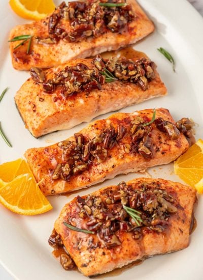 Salmon with pecans and maple syrup on a platter with oranges as garnish.
