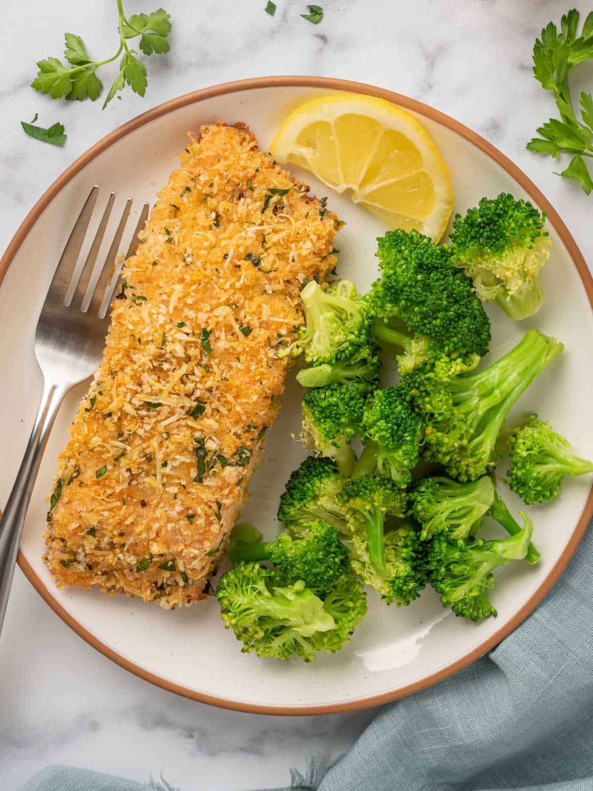 Crispy baked salmon on a plate with a fork and a pile of steamed broccoli.