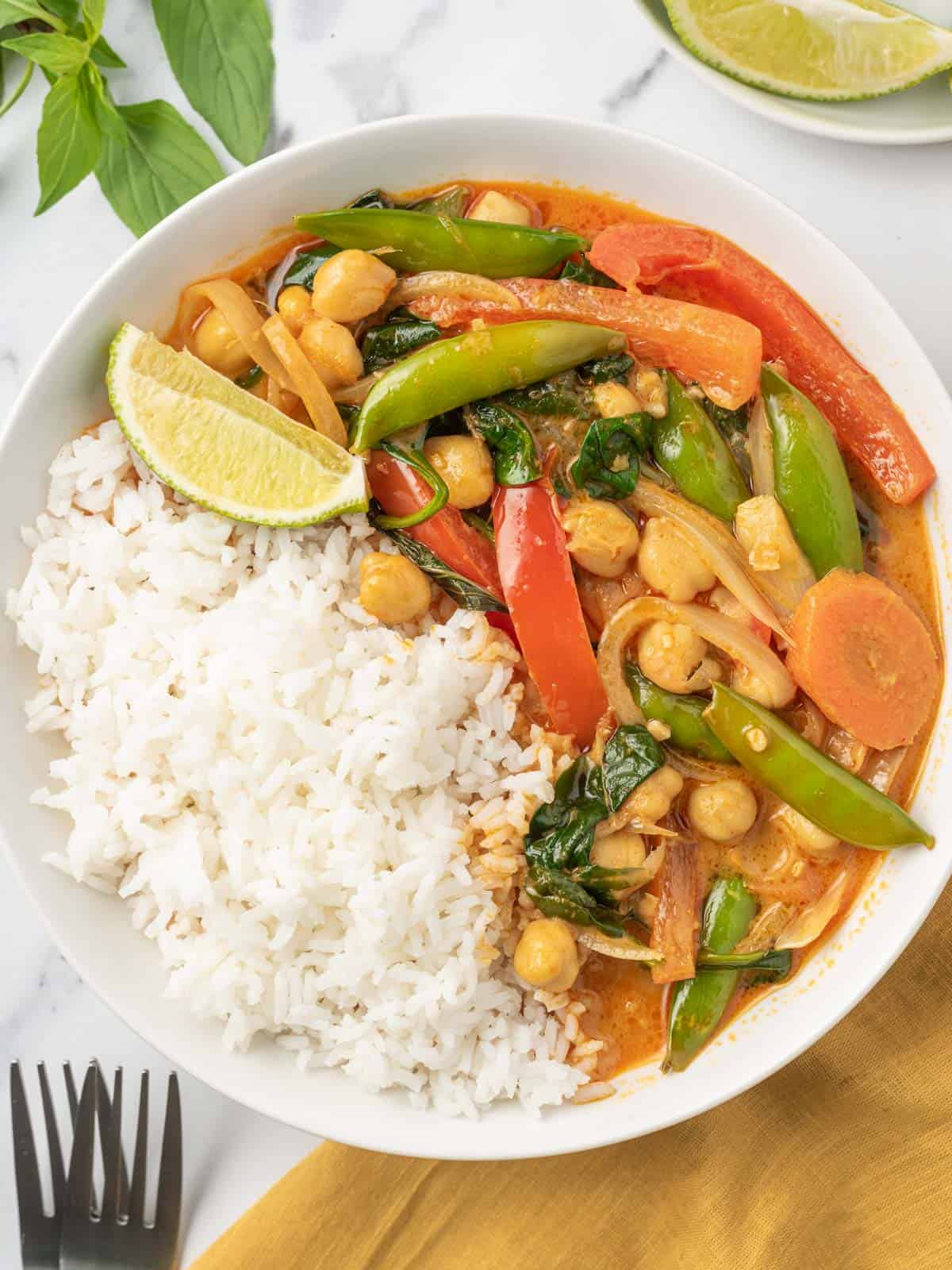 A bowl of rice topped with vegan red curry with vegetables.