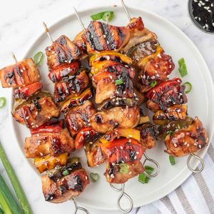 A pile of grilled chicken teriyaki skewers on a round platter.