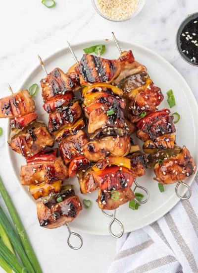 A pile of grilled chicken teriyaki skewers on a round platter.