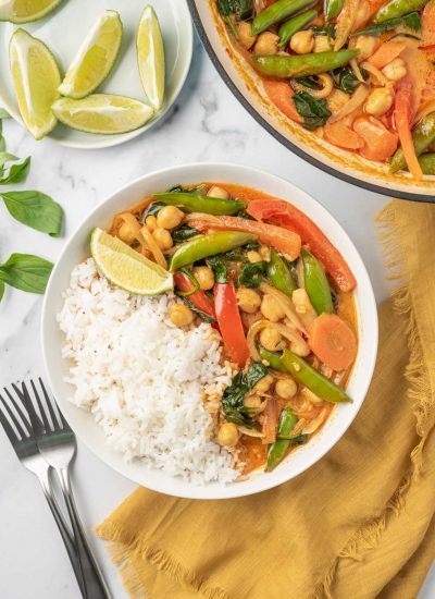 A bowl of rice with red thai curry and a pot of curry in the background.