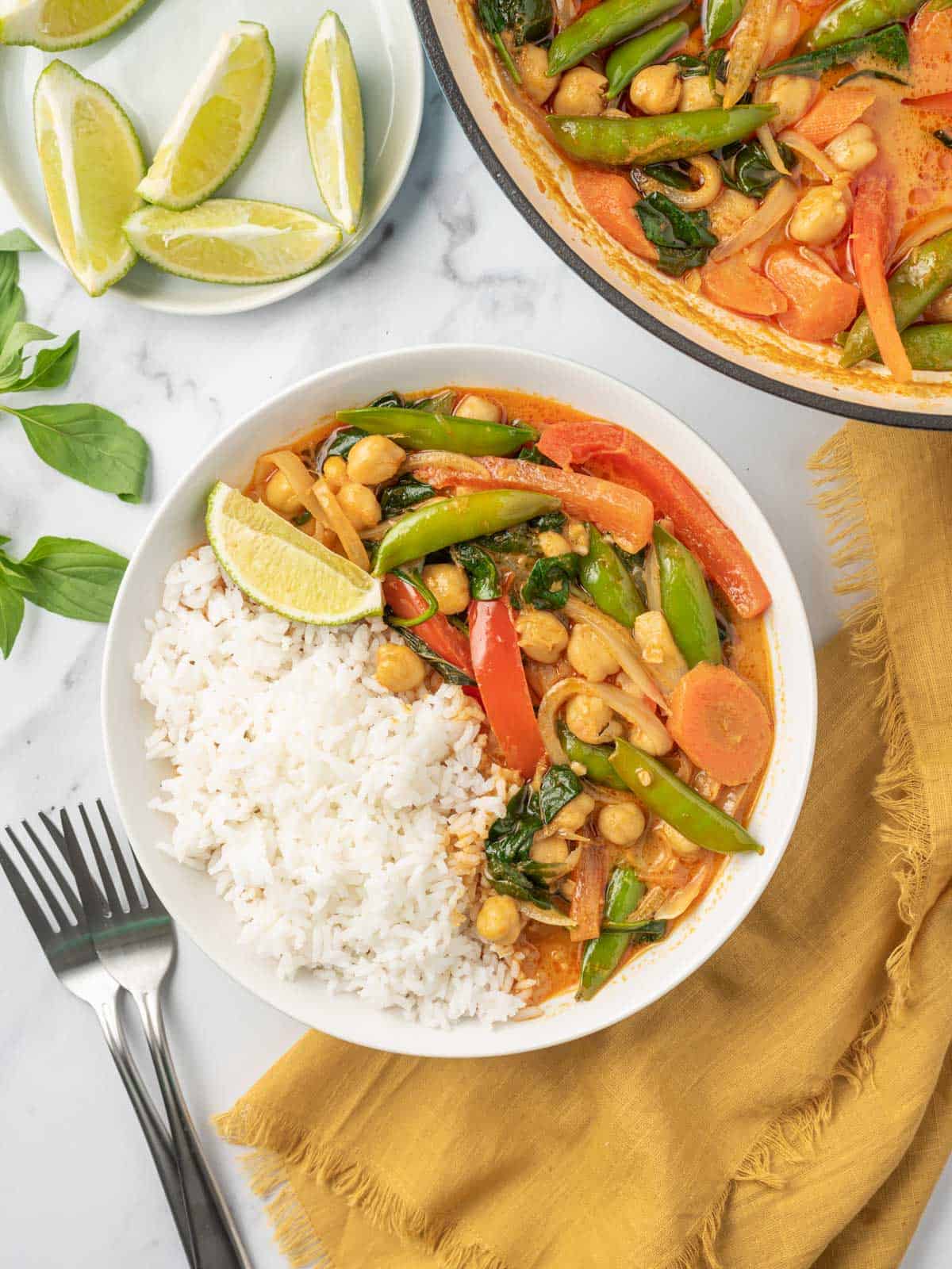 A bowl of rice with red thai curry and a pot of curry in the background.