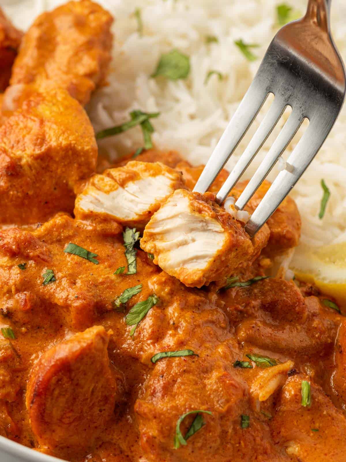 A fork holds a juicy piece of chicken tikka masala marinated chicken.