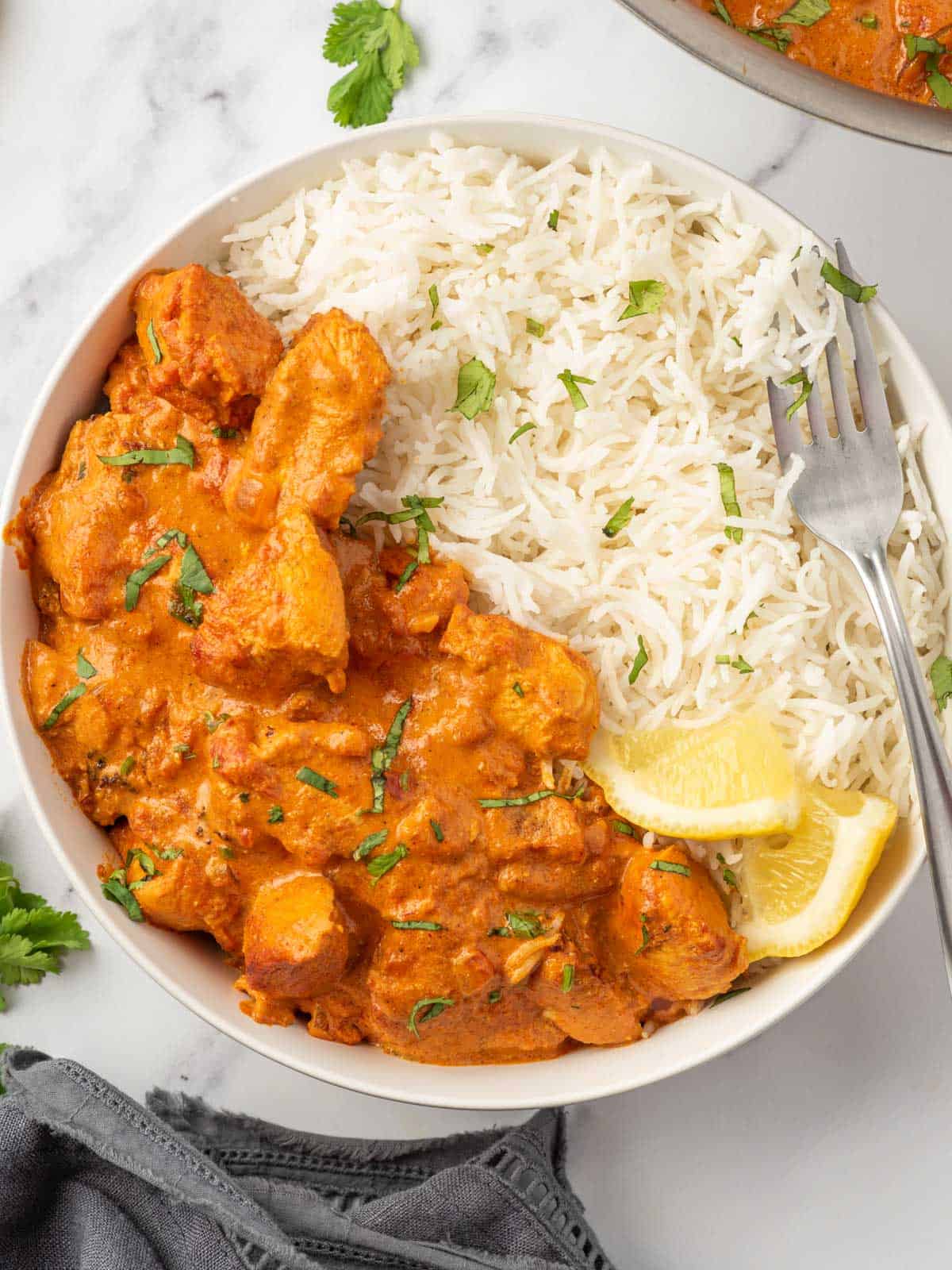 A fork rests on a bowl of healthy chicken tikka masala served with rice.