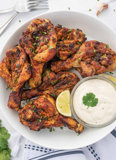 Butterfly drumsticks on a plate with a dipping sauce.