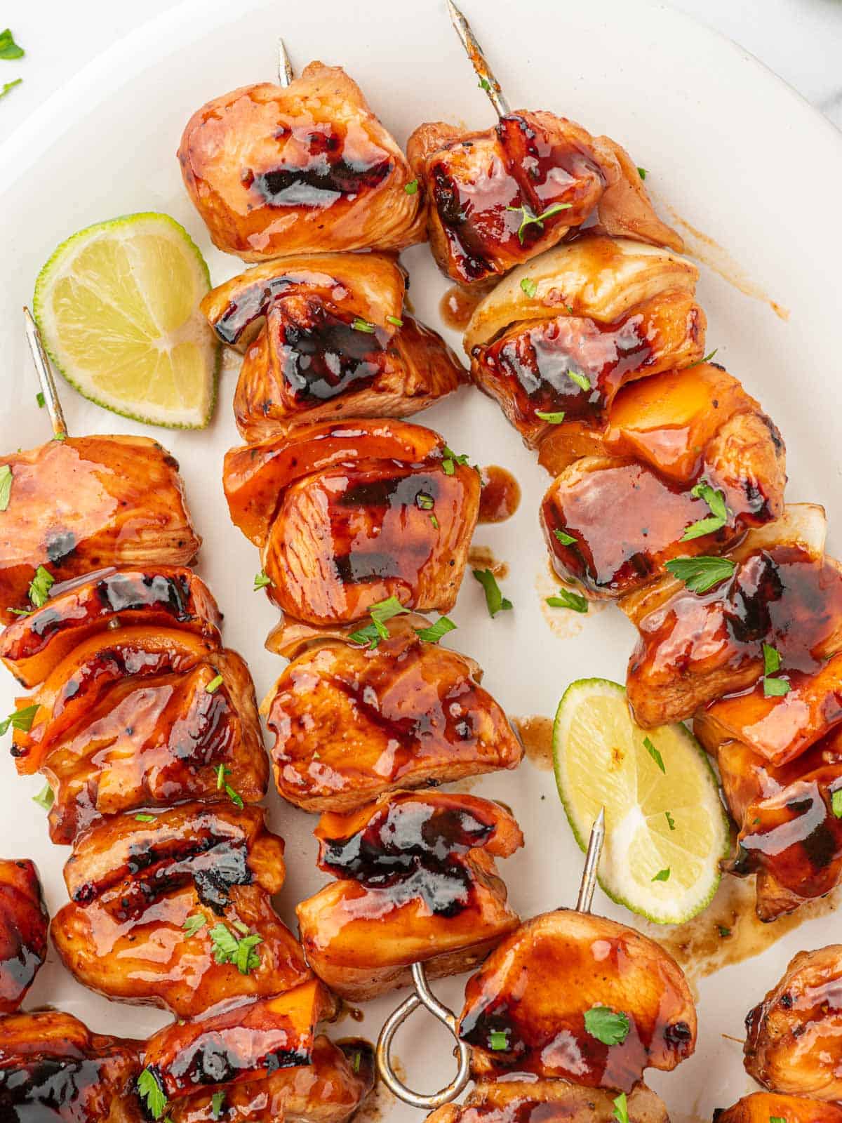 Cooked honey bbq chicken kabobs on a platter garnished with parsley and lime wedges.