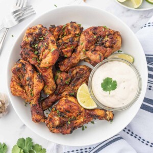 Air fryer butterfly chicken drumsticks on a plate with dipping sauce.