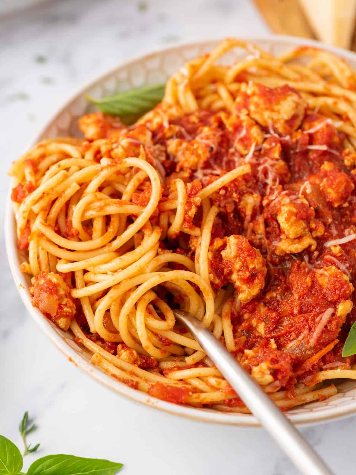 Closeup of a fork in a bowl of ground chicken bolognese.