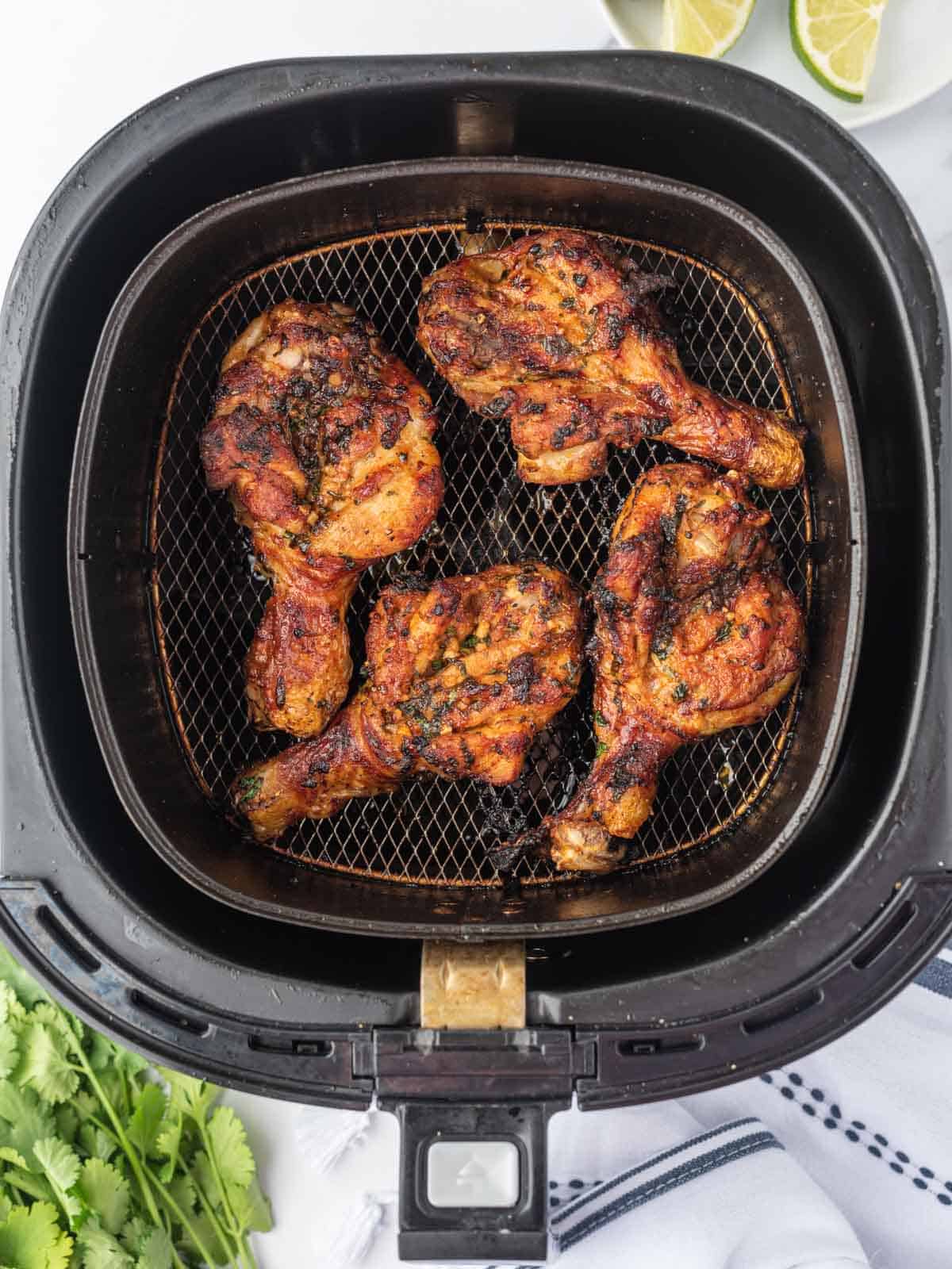 Butterfly drumsticks cooking in an air fryer basket.