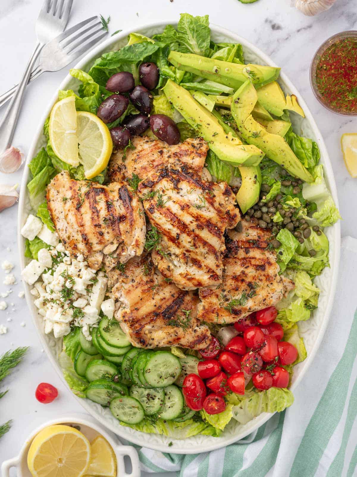 A large platter with grilled chicken greek salad.