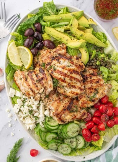 Greek chicken salad recipe on a platter with dressing on the side.