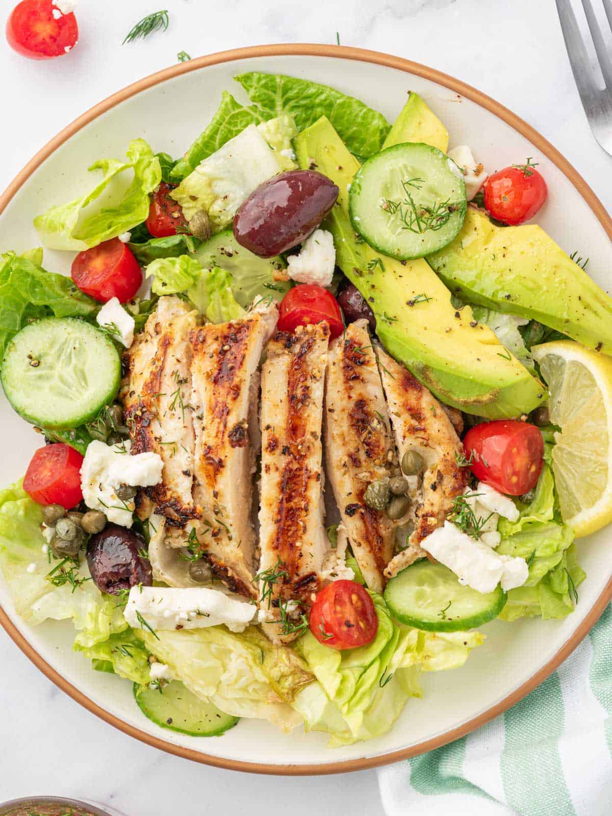 A plated portion of greek chicken salad with a fork and a napkin.