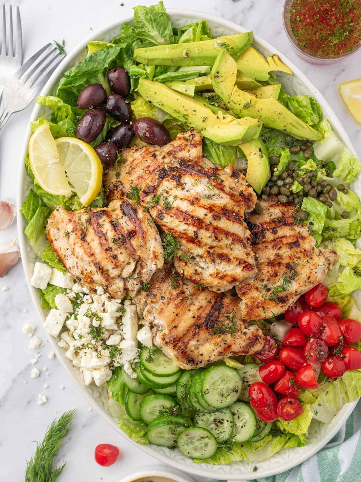 Greek chicken salad recipe on a platter with dressing on the side.