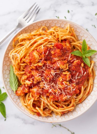 A bowl of healthy chicken bolognese garnished with fresh basil.