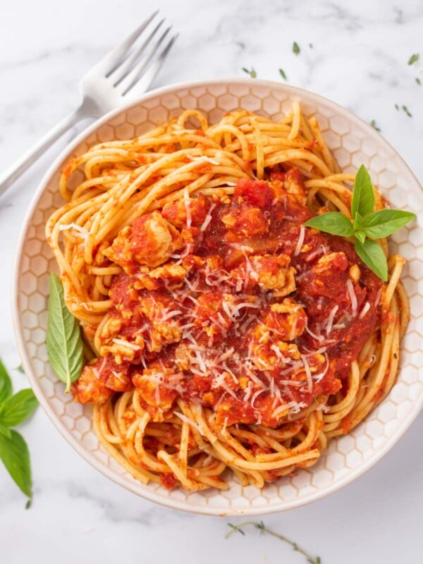 A bowl of healthy chicken bolognese garnished with fresh basil.