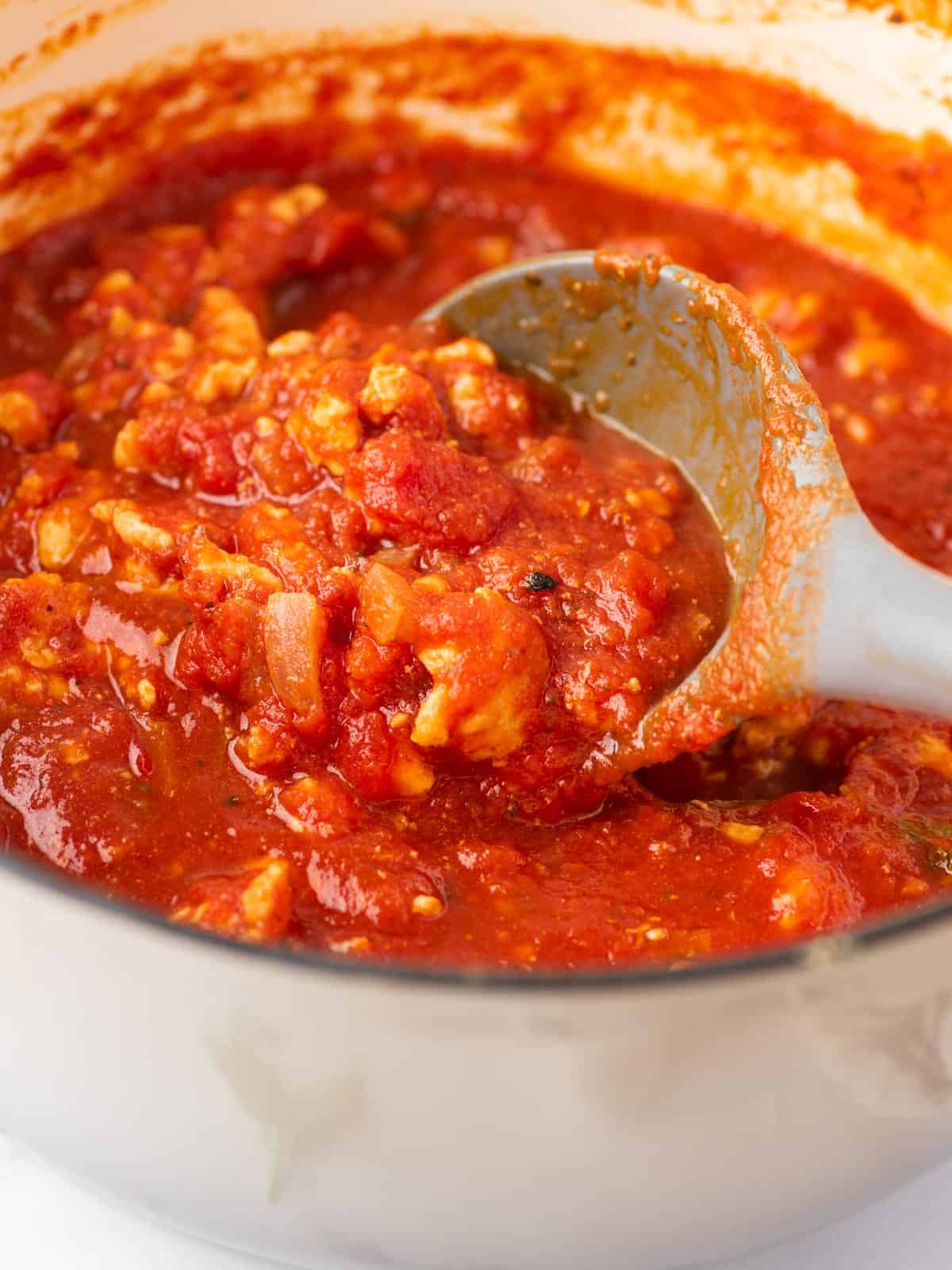 Spaghetti sauce with chicken in a saucepan being stirred with a spoon.