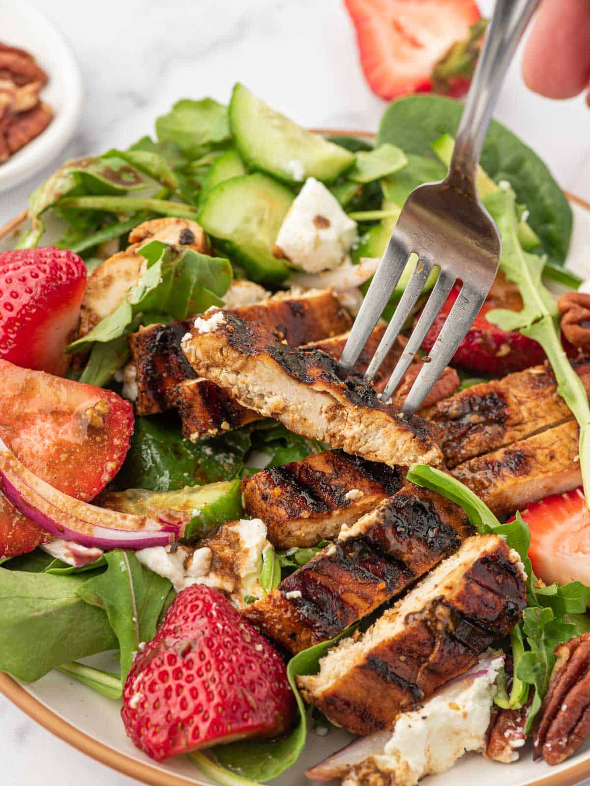 Balsamic grilled chicken on a fork over a plate of spinach and strawberry salad.