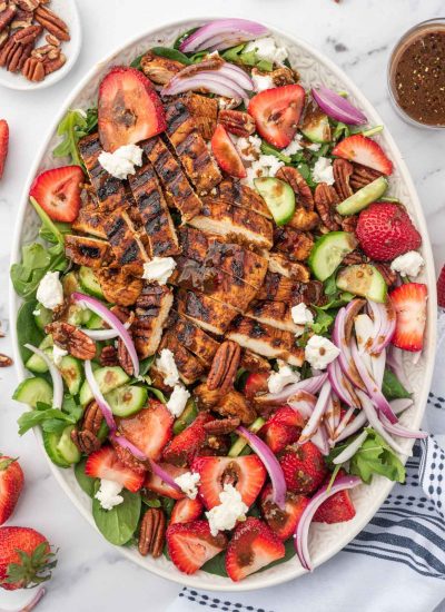 Grilled chicken on spinach salad with fresh strawberries on a serving platter with balsamic dressing and pecans to the side.