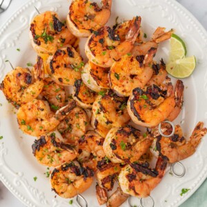 Honey lime shrimp skewers stacked on a plate with lime wedges.