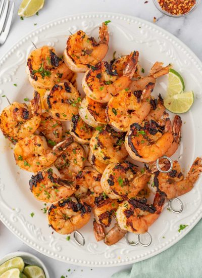 Honey lime shrimp skewers stacked on a plate with lime wedges.