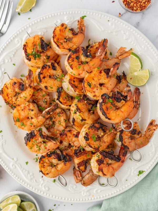 Honey lime shrimp skewers stacked on a plate with lime wedges.