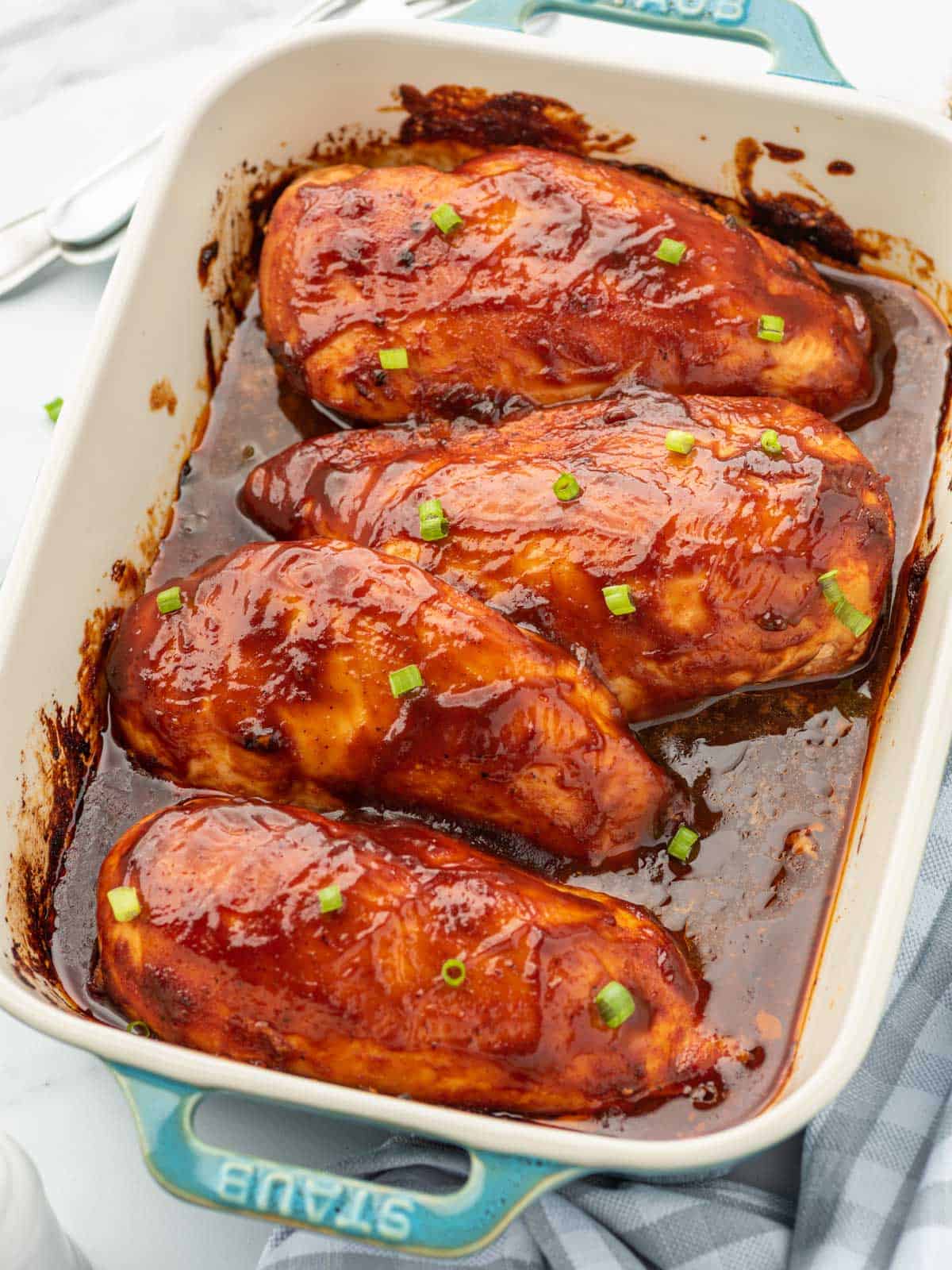 A casserole dish with 4 oven baked BBQ chicken breasts covered in sauce.