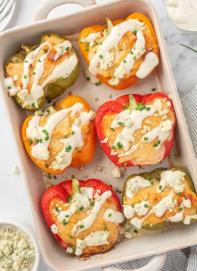 Healthy chicken stuffed peppers topped with ranch and crumbled blue cheese in a baking dish.