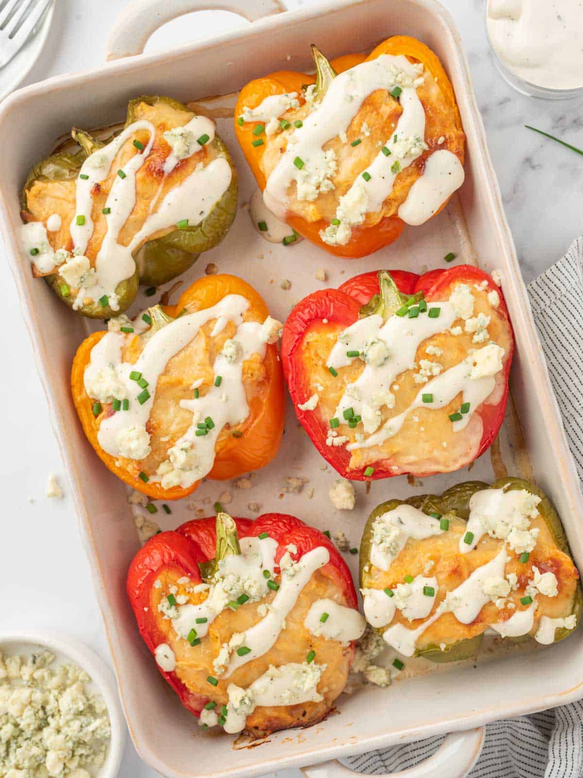 Healthy chicken stuffed peppers topped with ranch and crumbled blue cheese in a baking dish.