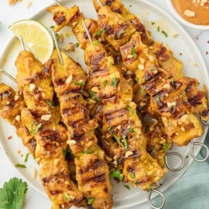 A pile of easy grilled chicken satay skewers on a platter.