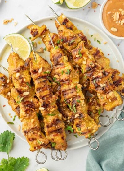 A pile of easy grilled chicken satay skewers on a platter.