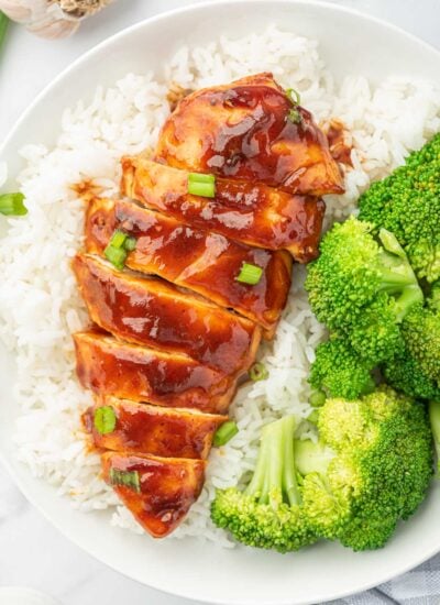 Sliced bbq chicken breast on a bed of rice with broccoli.
