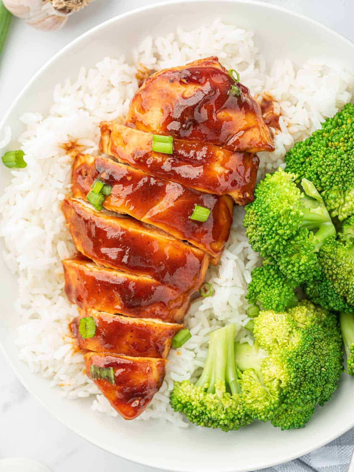 Sliced bbq chicken breast on a bed of rice with broccoli.