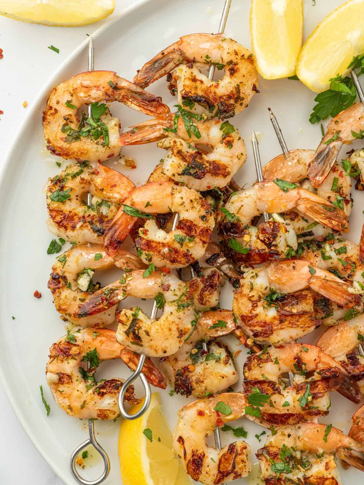 Shrimp kabobs with garlic on a white platter with lemon wedges.