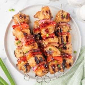 Grilled chicken kabob skewers on a plate garnished with sesame seeds.