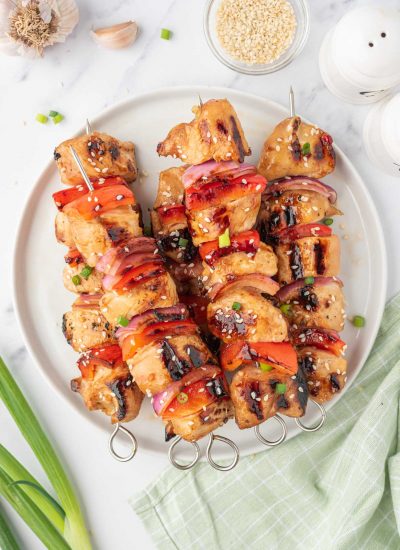 Grilled chicken kabob skewers on a plate garnished with sesame seeds.