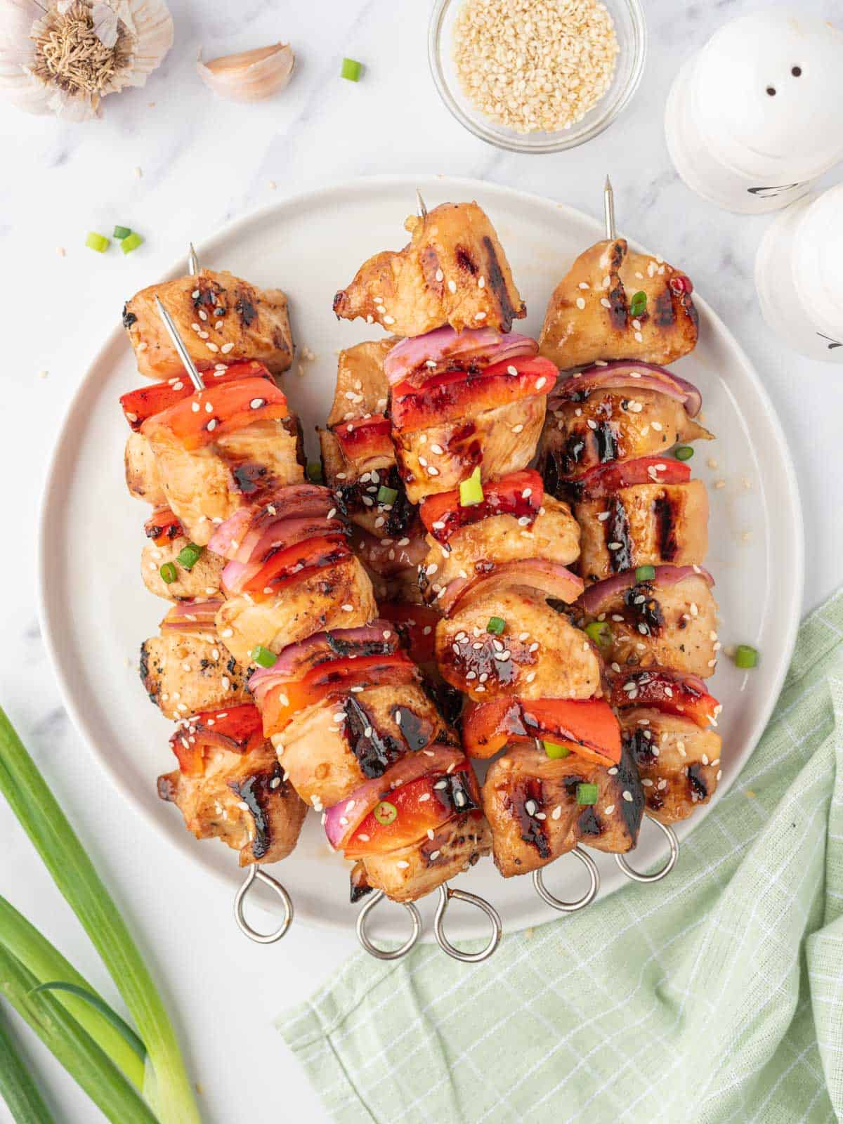 Grilled chicken kabob skewers on a plate garnished with sesame seeds.