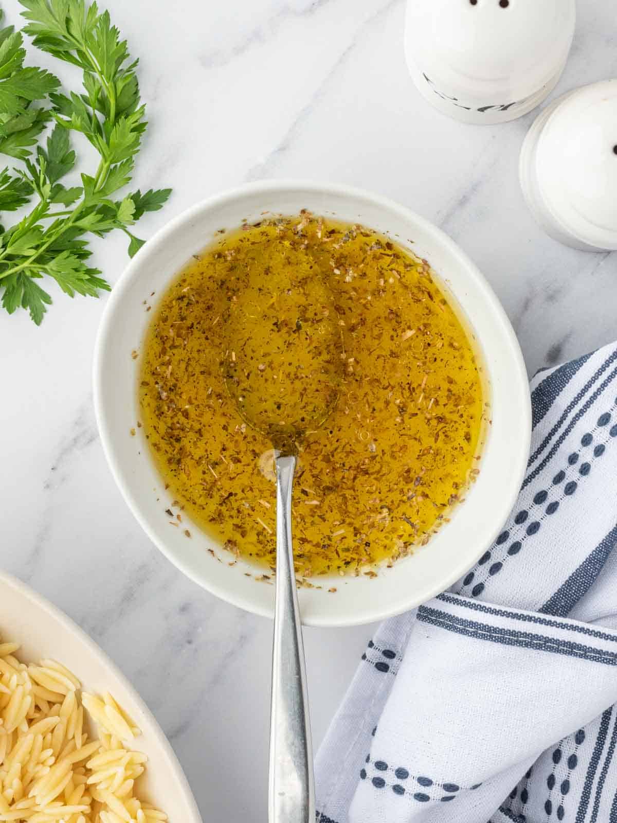 Mixing a lemony dressing for shrimp orzo salad in a bowl with a spoon.