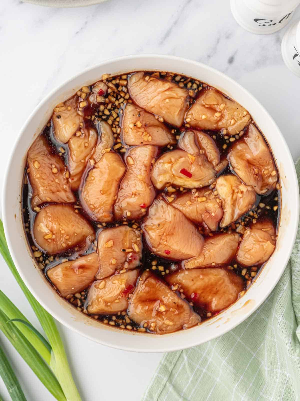 Pieces of cubed chicken marinating in a bowl of sauce.