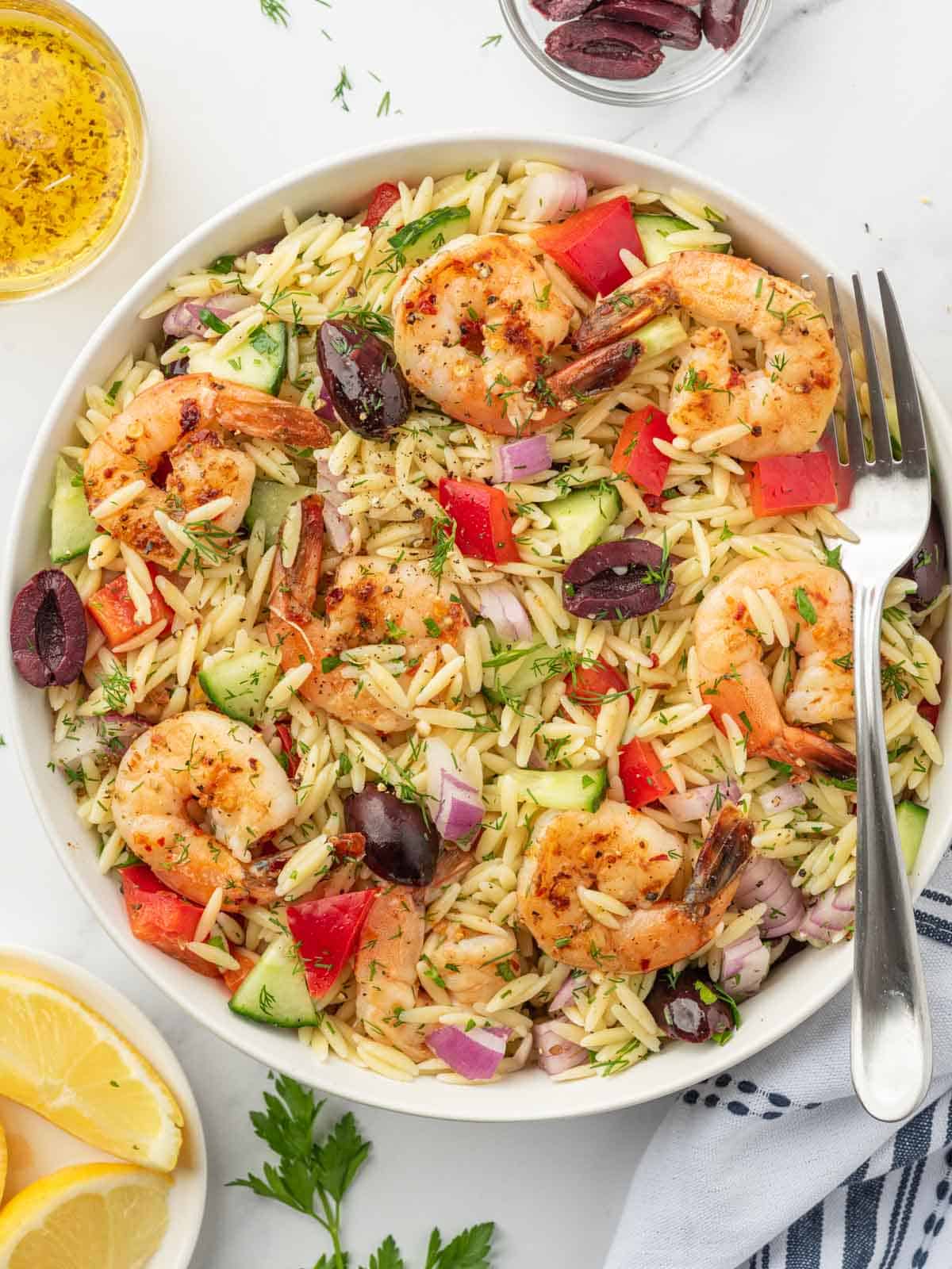 A fork rests on the side of a bowl of orzo salad with grilled shrimp.