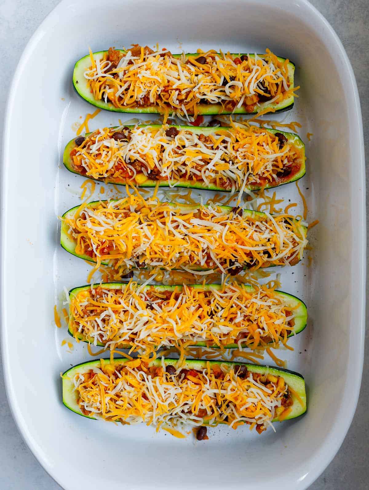 zucchini boats topped with shredded cheese before baking